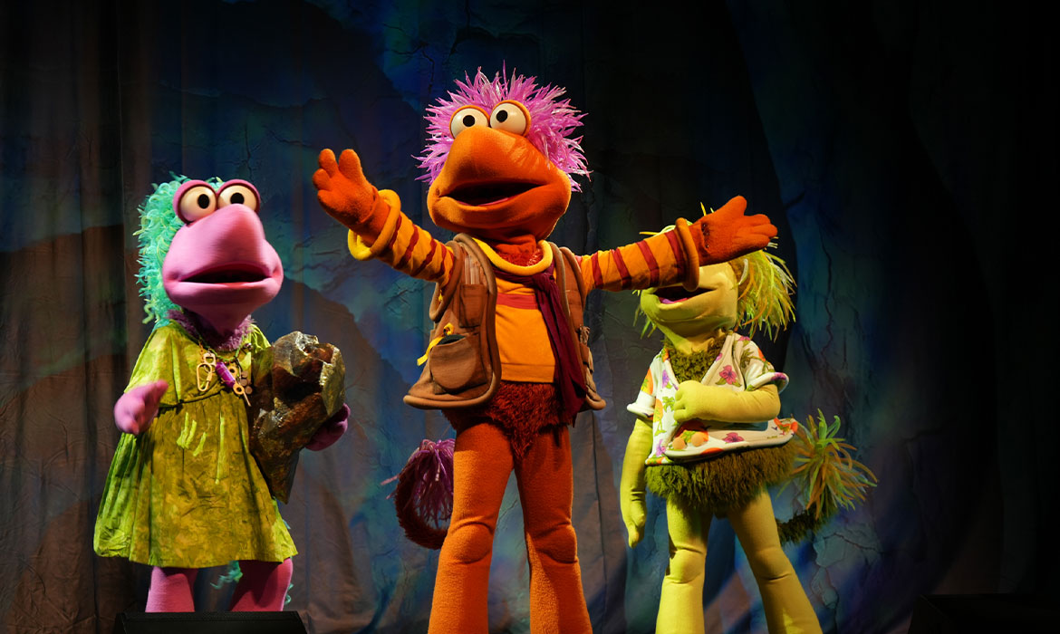 A colorful cast of Fraggles dances across the stage, surrounded by bright set pieces and playful lighting, bringing the joy, music and imagination of Fraggle Rock to life.